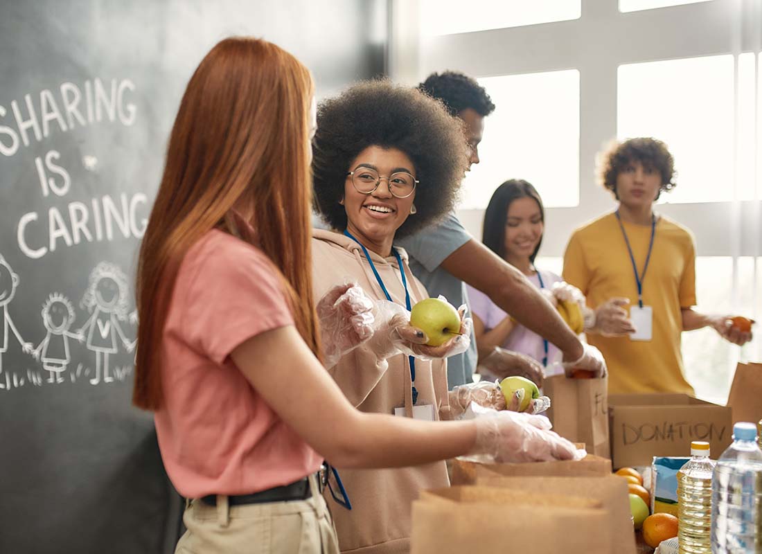 Non-Profit Insurance - Happy Young Volunteers Wearing Gloves and Collecting and Sorting Food While Working Together for Donations in a Charitable Organization