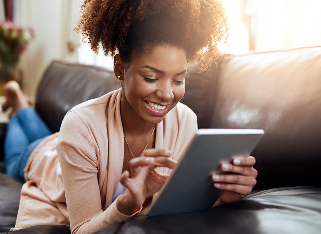 Gallen Sign Guys - Closeup View of a Cheerful Young African American Woman Laying on the Sofa at Home While Using a Tablet