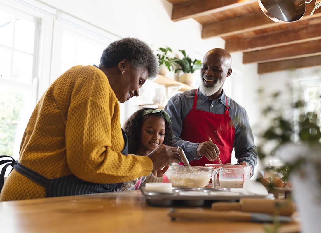 Insurance Solutions - Cheerful African American Grandparents Having Fun Baking with Their Young Graddaughter in the Kitchen