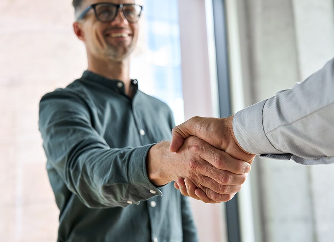 Our Partners - Closeup View of Two Business Men Shaking Hands While Standing in a Bright Office